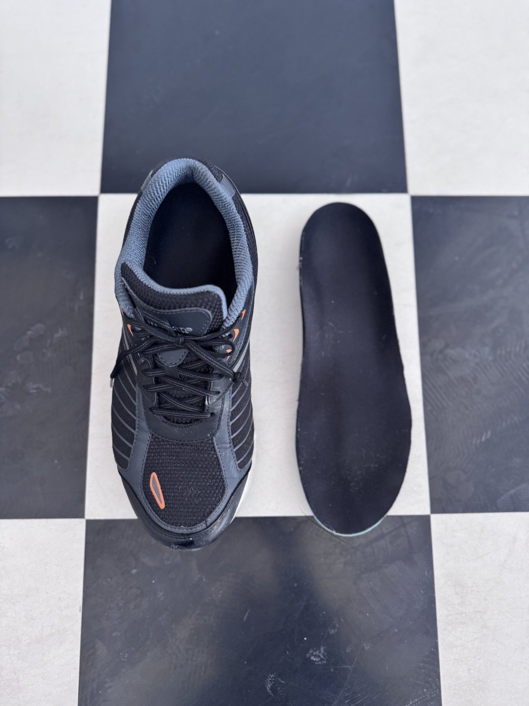 Black full length custom foot orthotic beside a supportive walking shoe