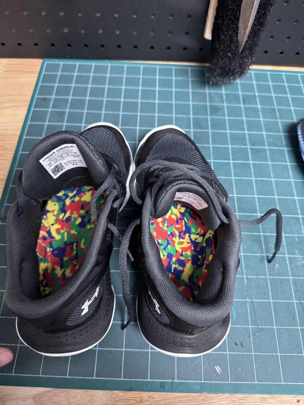 Pair of custom foot orthotics with colourful top covers inside black running shoes