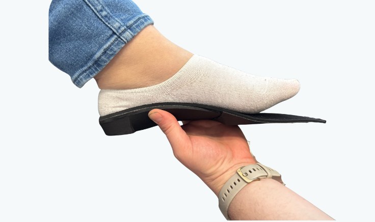 Hand holding a black custom foot orthotic under a foot