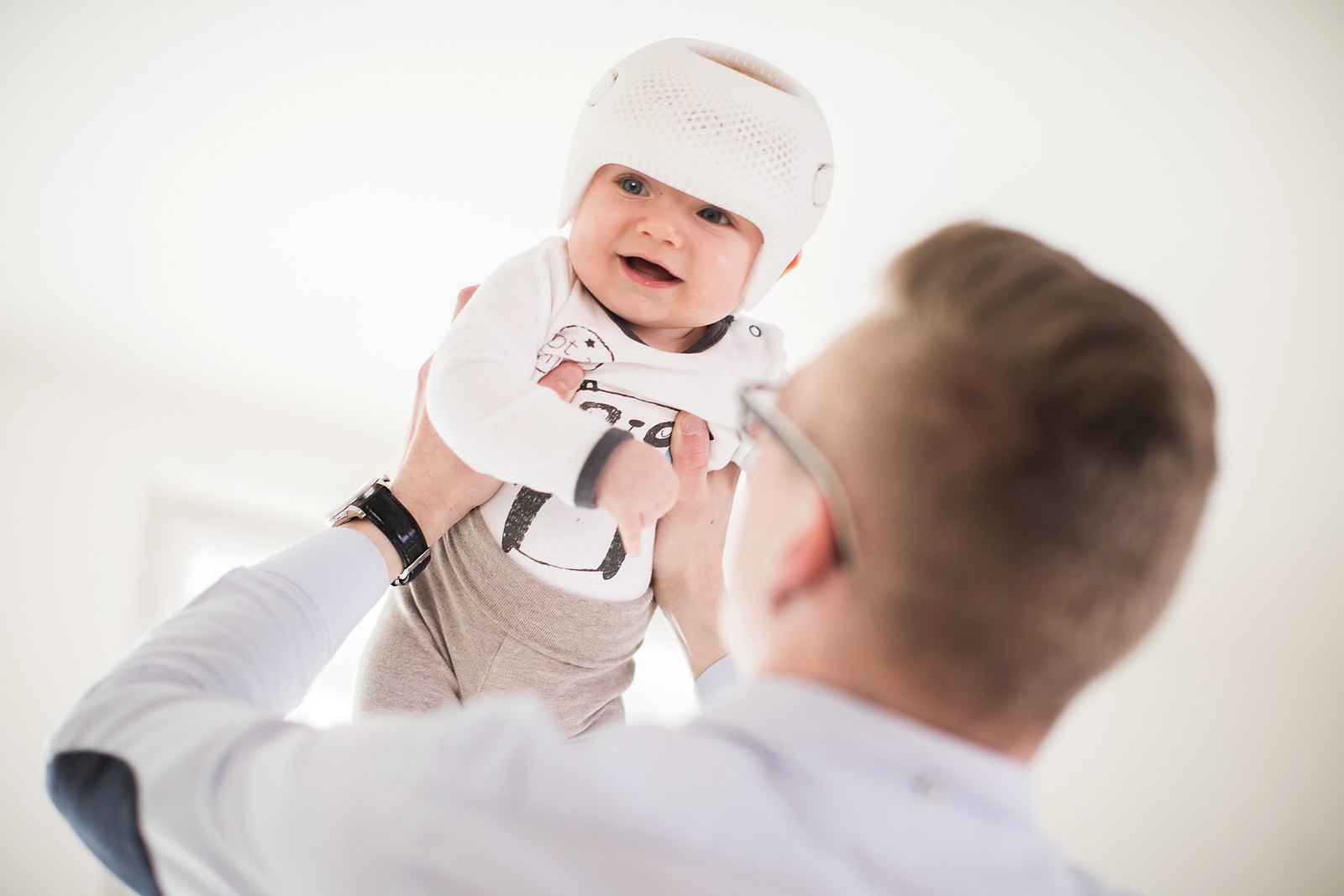 Smiling baby in a Talee helmet being lifted by a parent