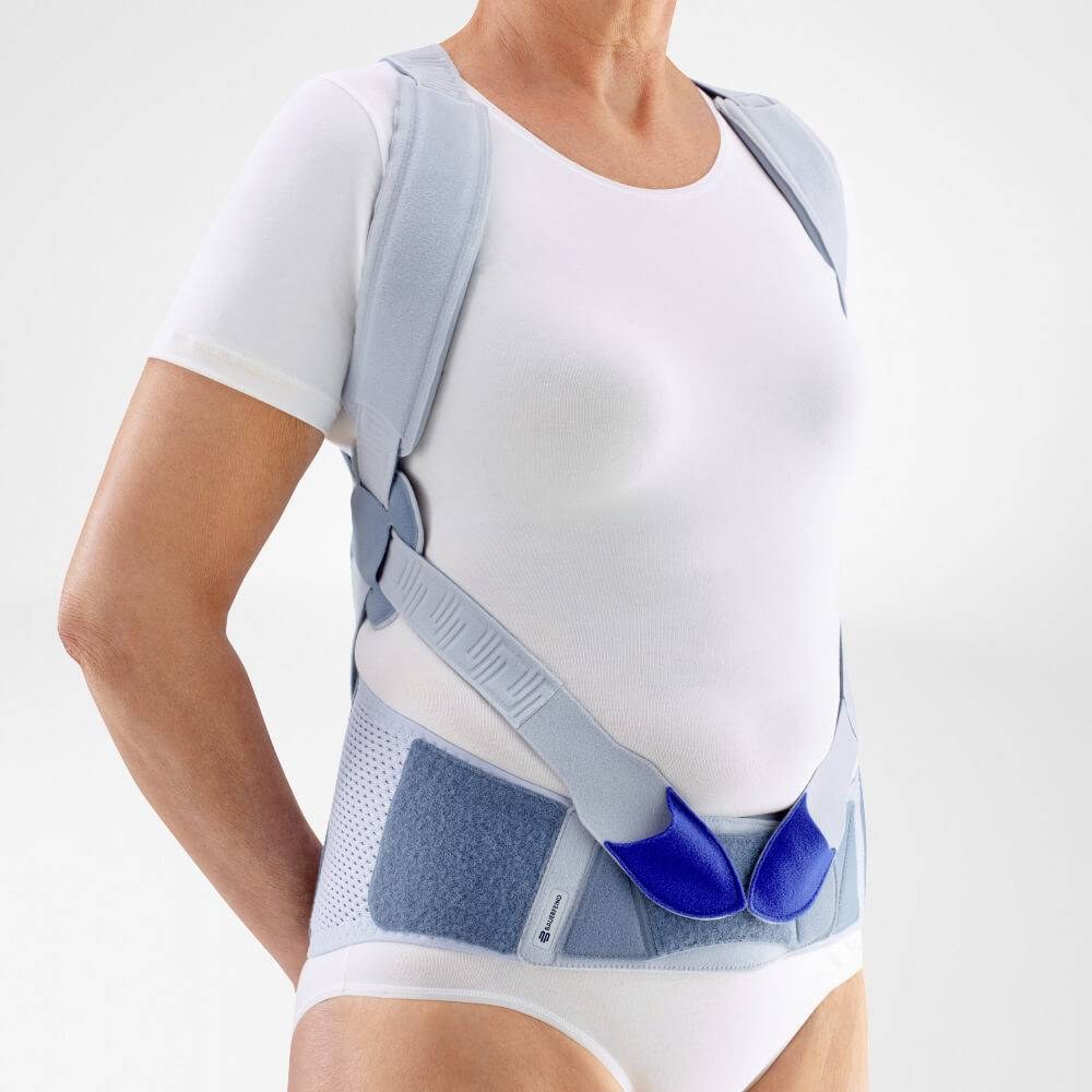 Front view of a woman wearing a posture back brace, showing the padded shoulder straps and pelvic belt